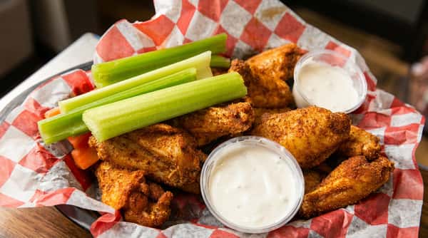 Chicken wings with celery sticks, baby carrots, and two cups of ranch dressing, served in a red and white checkered paper.