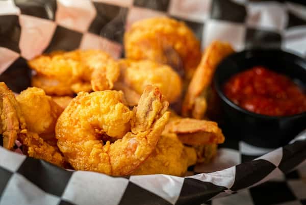 Fried shrimp in a black and white checkered paper basket with a side of red dipping sauce.