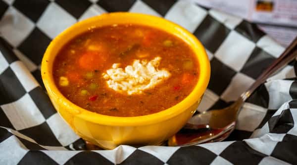 Vegetable soup with white cheese and a spoon in a yellow bowl on black and white checkered paper.