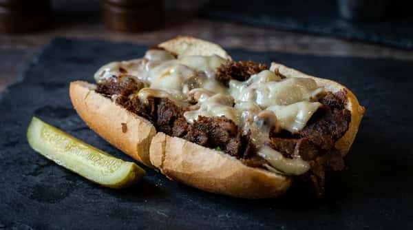 Cheesesteak sandwich with steak, melted cheese, and onions on a toasted roll, on a checkered paper-lined tray.