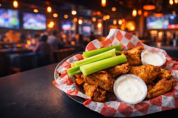 Basket of seasoned chicken wings served with creamy ranch dip, celery, and carrot sticks at The Upper Deck sports bar in Mount Airy, MD, offering classic American bar food favorites.