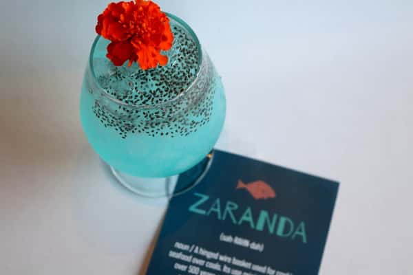 Signature craft cocktail garnished with a red flower, served alongside a Zaranda business card, a creative drink from Zaranda Houston's bar menu