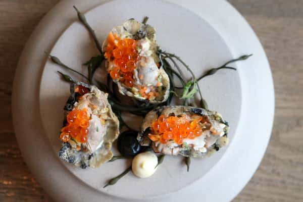 Soft Shell Oysters at Zaranda Houston, topped with vibrant roe and fresh herbs, served on a white plate, a refined seafood specialty