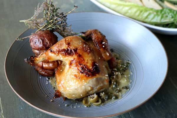 Pollo Rostizado jugoso con hierbas y especias, servido en plato oscuro, platillo del menú de Zaranda Houston