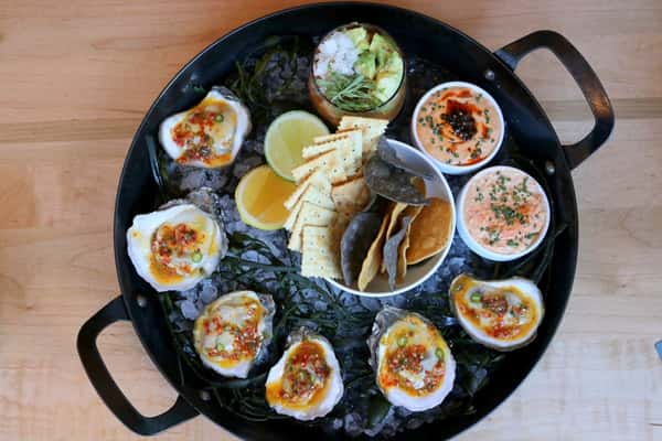 Plato de mariscos variados con ostiones, mejillones y otros frutos del mar frescos, presentados en un plato oscuro, parte del menú de Zaranda Houston