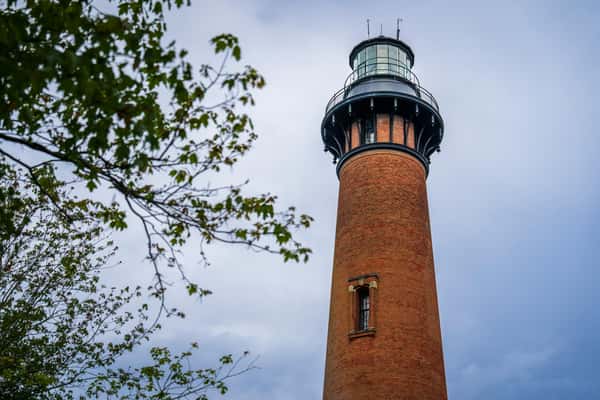 A tall brick lighthouse stands against a cloudy sky near The Salty Rim, a fun beach restaurant.