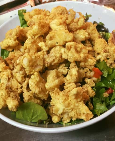 deep fried calamari topped over a bed of lettuce in a bowl