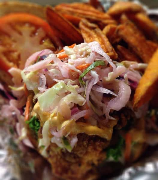 poboy topped with coleslaw, with a tomato and a side of sweet potato fries