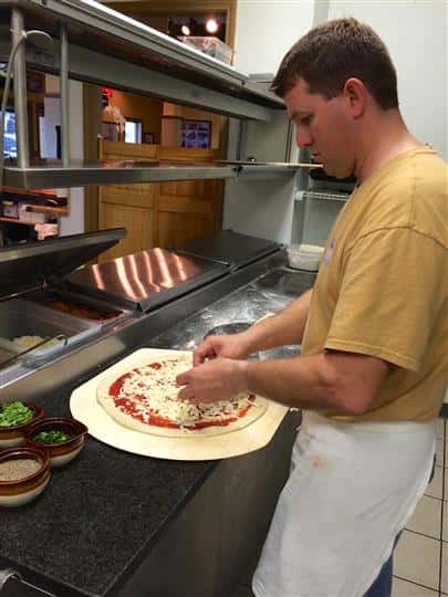 Worker Making Pizza By Putting Toppings on
