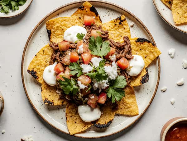 Loaded tostada-style nachos topped with shredded beef, pico de gallo, crema, queso fresco, and fresh cilantro.