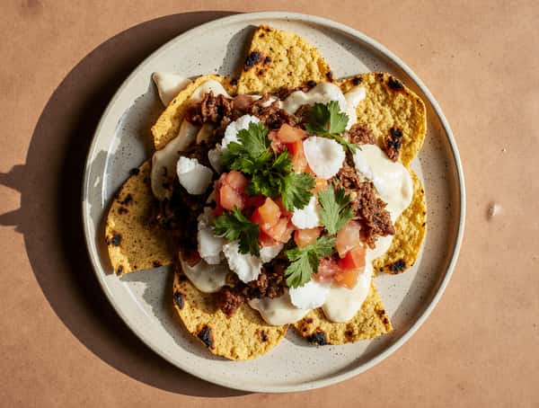 Mexican tostadas topped with shredded beef, queso fresco, crema, diced tomatoes, and fresh cilantro.