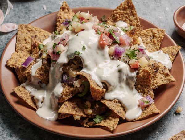 Loaded nachos topped with seasoned meat, pico de gallo, cilantro, and creamy queso sauce on crispy tortilla chips.