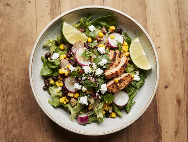 Fresh Mexican salad with grilled chicken, corn, black beans, radish slices, queso fresco, and lime wedges.