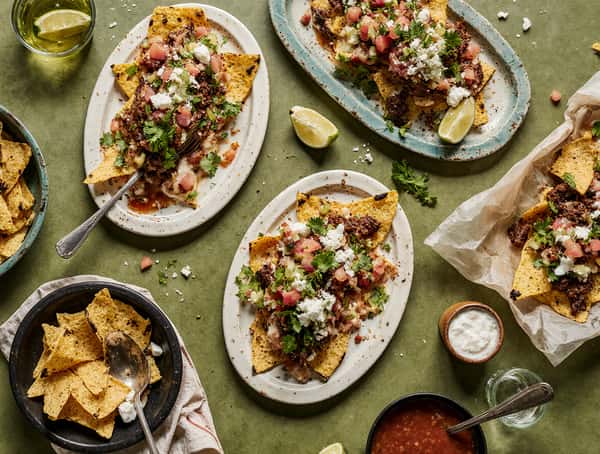 Mexican nacho platters topped with shredded beef, diced tomatoes, queso fresco, cilantro, and crema served with lime wedges.