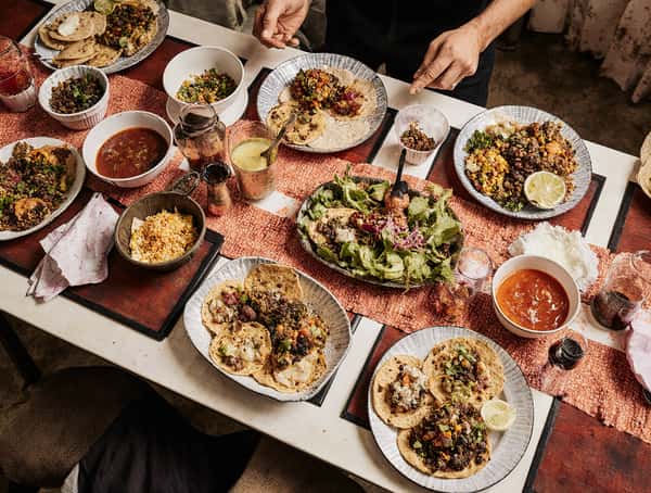 Family-style Mexican dinner spread with tacos, salads, salsa bowls, and shared plates on a large dining table.