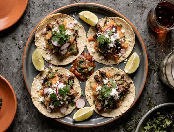 Plate of authentic street tacos with grilled meat, radish, cilantro, queso fresco, and salsa served with lime.