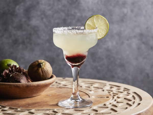 Craft margarita cocktail with salted rim, lime wheel garnish, and layered fruit puree served on a decorative table.
