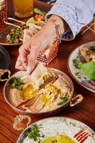 A hand reaching down to scoop hummus on to pita