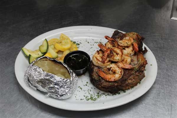 steak topped with cooked shrimp with a baked potato and vegetables