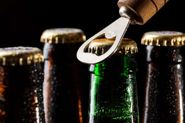 Close up of beer caps being opened with a bottle opener