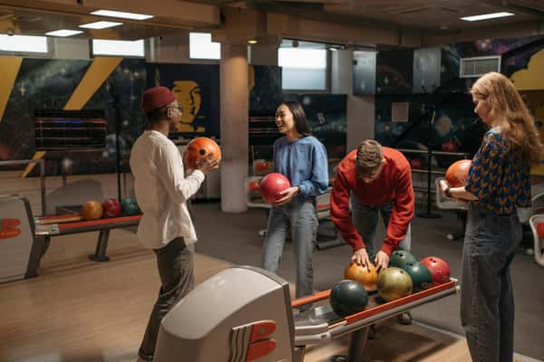 Group of friends at a bowling alley smiling and picking out bowling balls before their game.