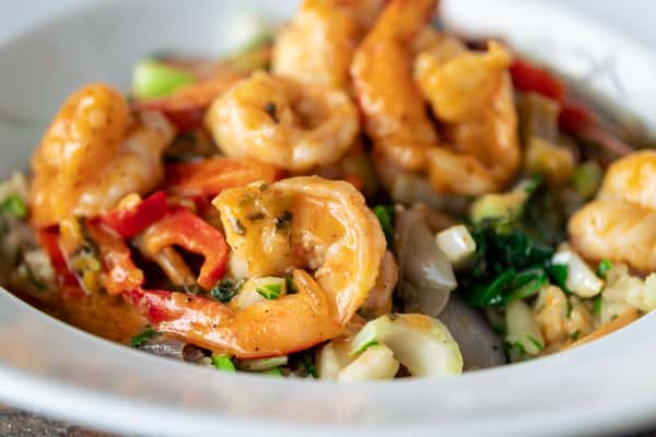 Vibrant orange shrimp with red bell peppers and green vegetables in a golden sauce, served on a white plate.