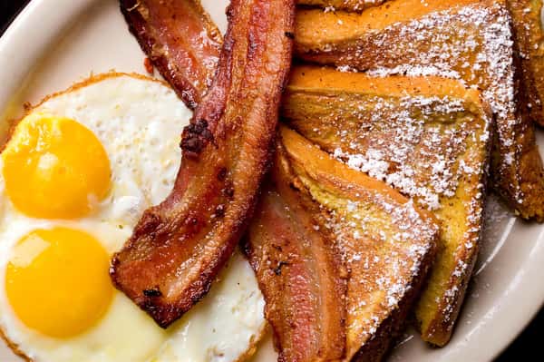 Two eggs over easy with strips of bacon and French toast with powdered sugar