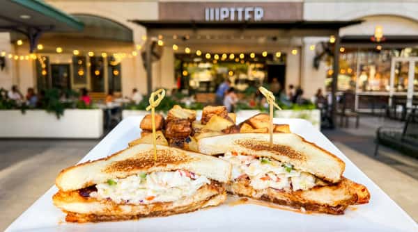 Fried chicken sandwich with coleslaw and BBQ sauce, served with roasted potatoes on a white plate.
