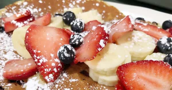 Close up of pancake with fruit on top with powdered sugar
