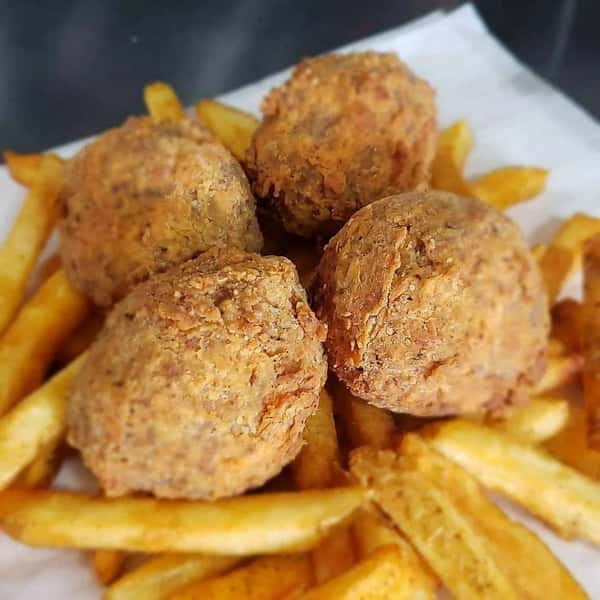 Crispy hush puppies served with seasoned fries on white parchment, featuring a golden-brown crust.
