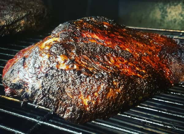 Whole smoked brisket with a dark, glistening bark resting on a grill inside a smoker, showcasing authentic Texas barbecue style.