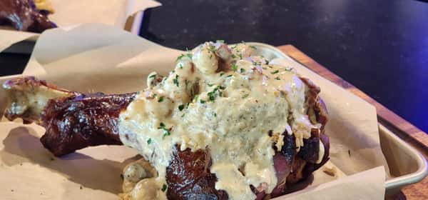 Smoked turkey leg topped with creamy Cajun shrimp sauce, served on parchment-lined tray with fresh herbs.