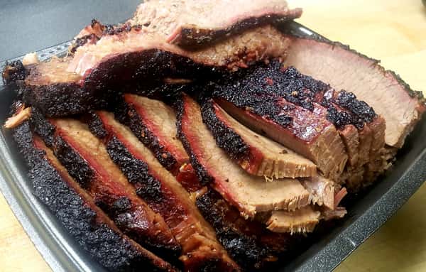 Tender slices of Texas-style smoked brisket with a blackened bark and visible smoke ring, stacked in a serving tray.