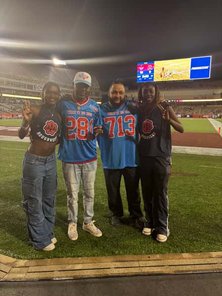 Group of fans wearing Houston Roughnecks football gear posing on the field at night in a stadium setting.