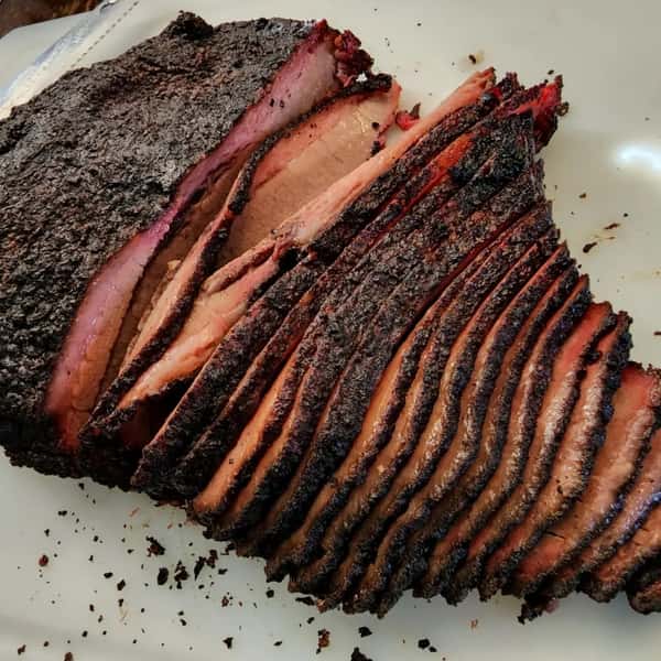 Beautifully sliced smoked brisket with a dark bark crust and juicy interior, laid out on a white cutting board.