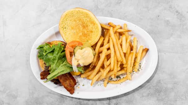 Coaches Corner's crispy bacon burger with fresh lettuce, tomato, and pickles, served alongside golden french fries on a white plate.