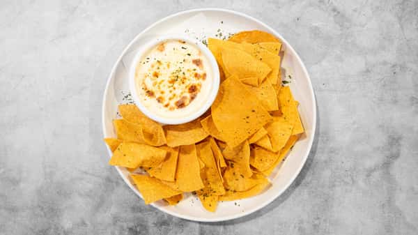 Coaches Corner's warm, creamy cheese dip with crispy golden tortilla chips, garnished with herbs.