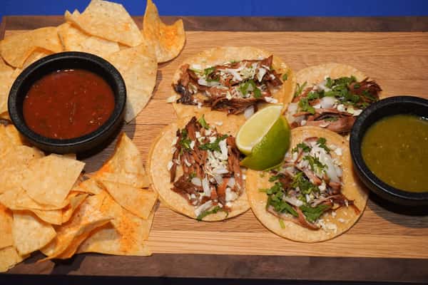 Authentic Mexican street tacos topped with seasoned meat, fresh cilantro, onions, and queso fresco, served with tortilla chips, salsa, and a lime wedge.