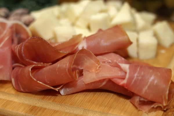 Prosciutto deli meat thinly sliced and diced provolone on a wooden cutting board
