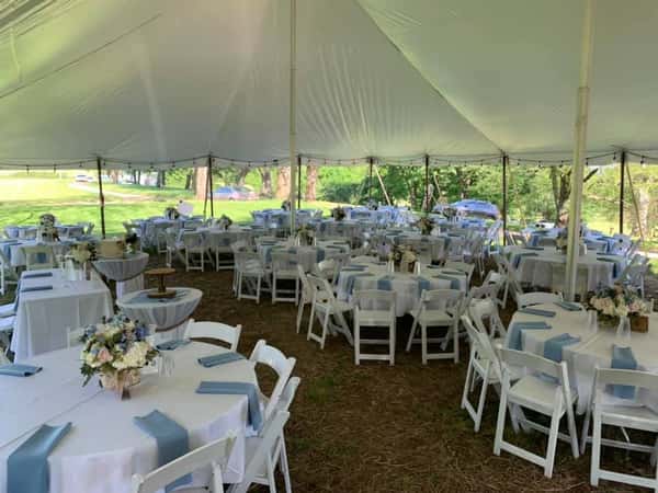 Many tables set with linen and chairs under a tent at a catering event