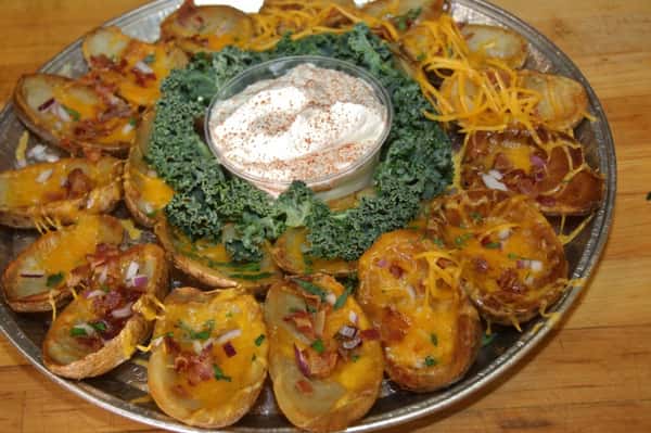 Loaded baked potatoes topped with cheddar cheese and bacon with sour cream in the middle of the platter