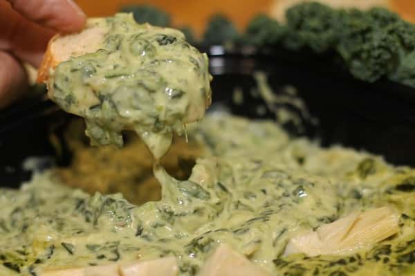 A hand dipping bread into spinach and artichoke dip