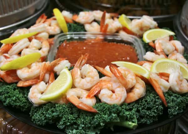 Shrimp surrounding a plastic container of cocktail sauce on a platter