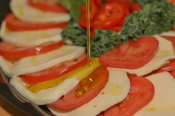 A mozzarella and tomato platter with olive oil dripping on top of it