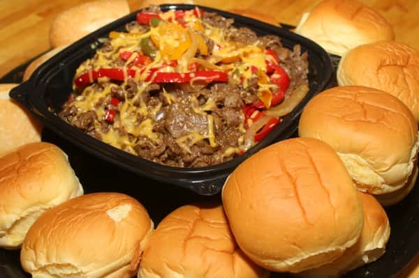 A philly cheesesteak platter for a catering event which consists of philly cheesesteak ingredients in the center of a tray surrounded by rolls