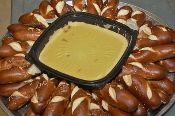 A tray containing a bowl of melted cheese surrounded by pretzel bread