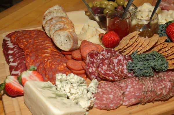 A charcutier board filled with crackers, salami, pastrami, pepperoni, various cheeses, fruit, bread, and jam