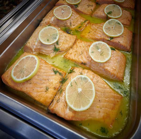 Assortment of grilled salmon topped with lemon slices in a tray