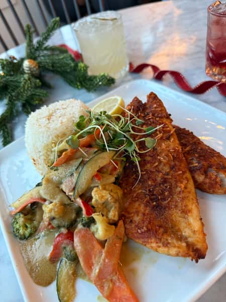 blackened fish fillet with jasmine rice and sautéed vegetables in creamy sauce, served with cocktails in a modern restaurant setting
