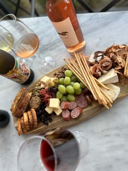 charcuterie board with assorted cheeses, cured meats, grapes, crackers, and bread served with glasses of rosé and red wine